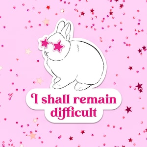 Op de afbeelding: Een witte sticker met een zwarte omtrek van een konijn dat een felroze, stervormige zonnebril draagt. Onder het konijn staat in een witte tekstballon de tekst I shall remain difficult in een vetgedrukt, donkerroze schreefloos lettertype.