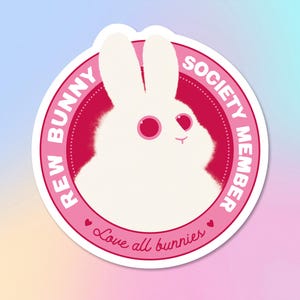 Könnte beinhalten: Ein runder Aufkleber mit einer weißen Hasenillustration in einem rosa Kreis. Der Text "REW BUNNY SOCIETY MEMBER" und "Love all bunnies" ist auf dem Aufkleber gedruckt.