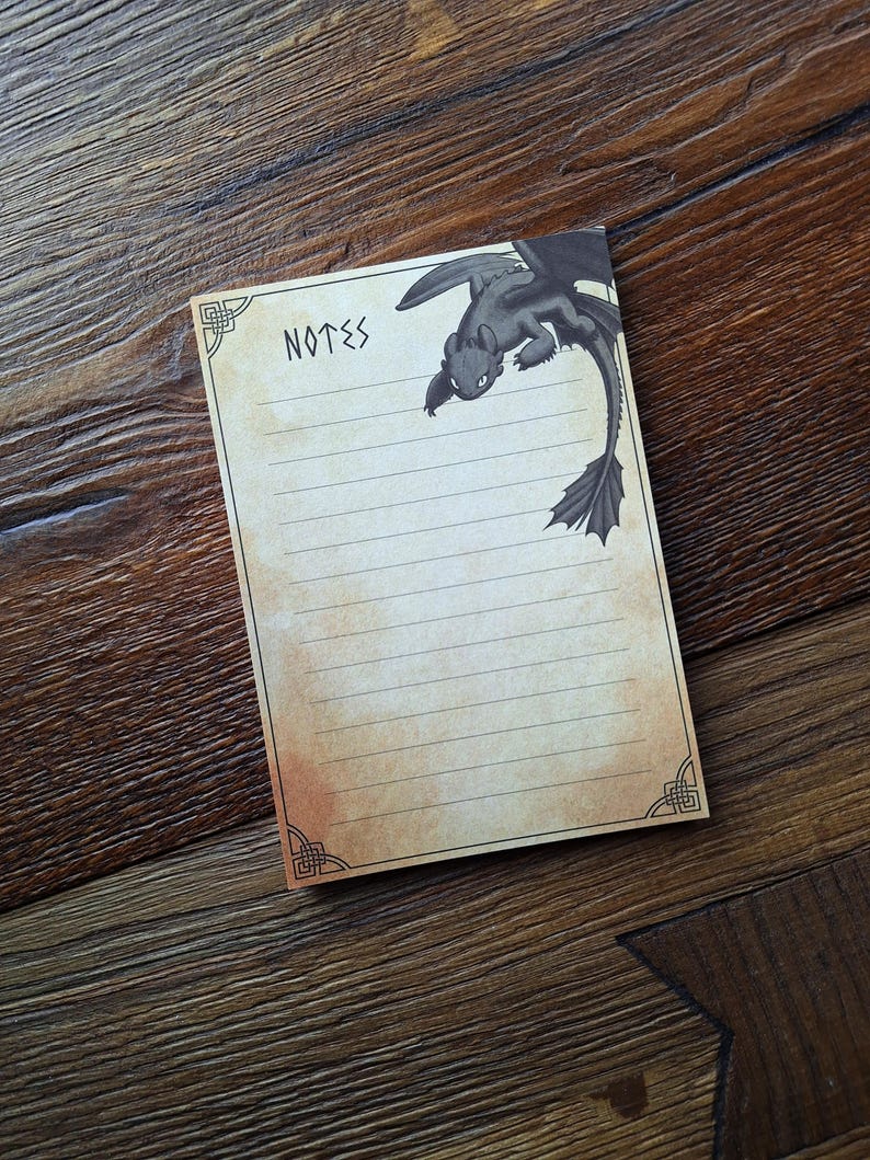 May include: A lined notepad with the word "NOTES" at the top and a black dragon illustration. The notepad has a vintage, aged paper appearance with decorative corner designs. The dragon illustration is black.