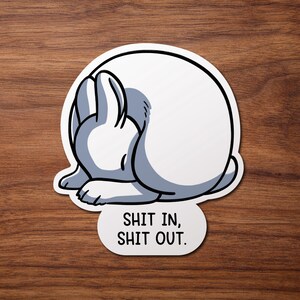 May include: White rabbit curled up in a ball with the text "Shit in, Shit out." printed below.