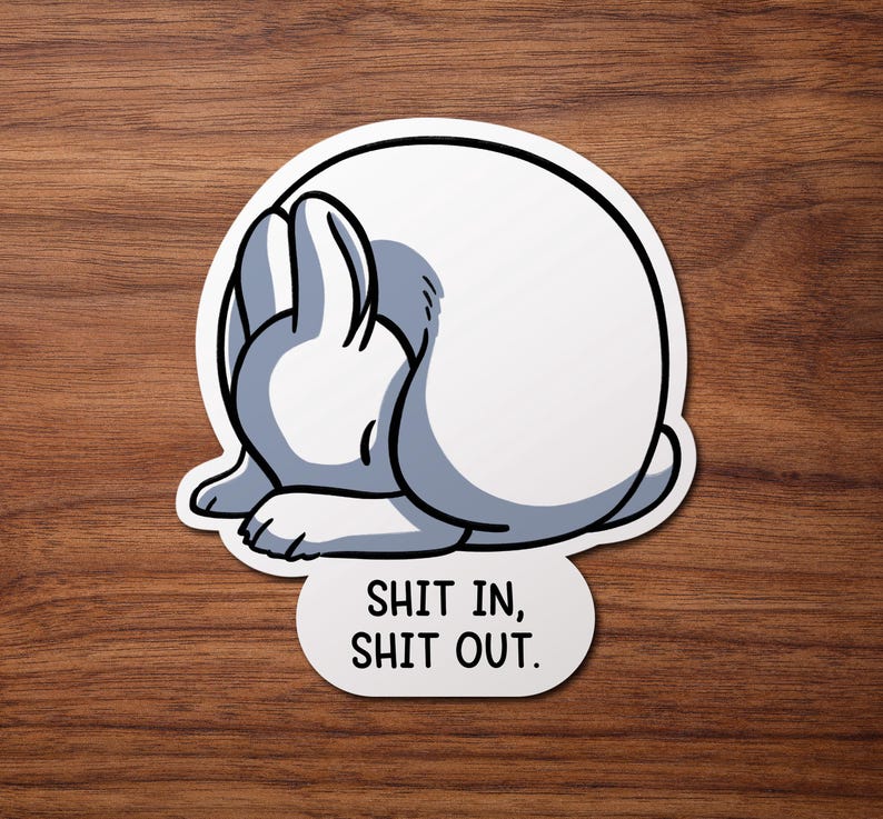May include: White rabbit curled up in a ball with the text "Shit in, Shit out." printed below.