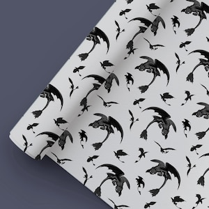 Peut inclure: Un rouleau de papier cadeau gris clair avec un motif répétitif de silhouettes de dragons noirs dans diverses poses de vol. Le design comprend des illustrations détaillées de dragons avec de grandes ailes et de longues queues.