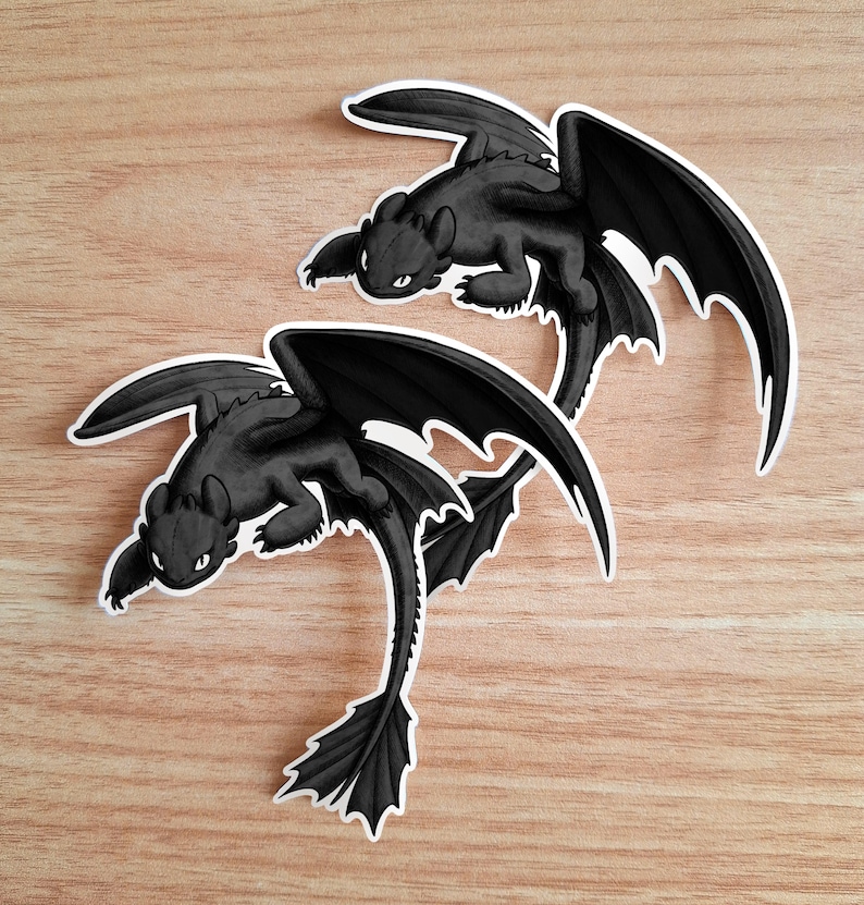 Puede incluir: Dos pegatinas negras de drag&oacute;n con contornos blancos se muestran sobre una superficie de madera marr&oacute;n claro. Los dragones tienen alas grandes, orejas puntiagudas y una cola larga. Las pegatinas est&aacute;n en una pose de vuelo.