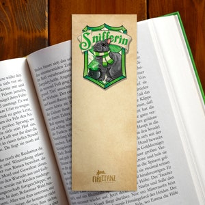 May include: A green and gold bookmark with a black and white illustration of a cat wearing a green scarf and holding a cauldron. The text "Snifferin" is written in green letters on the bookmark.