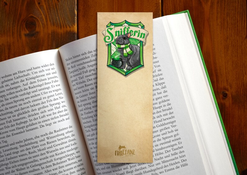 May include: A green and gold bookmark with a black and white illustration of a cat wearing a green scarf and holding a cauldron. The text "Snifferin" is written in green letters on the bookmark.