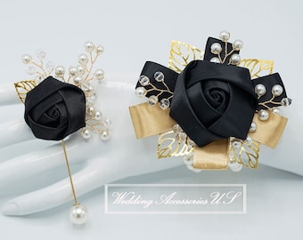 May include: Two black rose corsages with gold accents and pearl embellishments. One corsage is a pin-on style with a long gold pin and a large pearl. The other is a wrist corsage with gold ribbon and a black bow.