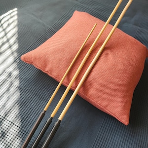 May include: Three wooden rods with black handles, of varying lengths, are arranged on a red pillow on a blue textured surface.