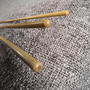 Puede incluir: Tres varillas de madera, probablemente para una caña de pescar, se muestran sobre una superficie de tela texturizada. Las varillas son de bambú natural y tienen un color marrón claro.