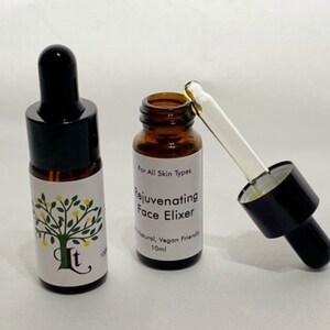 May include: Two amber glass bottles with black dropper tops. The bottle on the right has a clear dropper and is labelled "Rejuvenating Face Elixir" with the text "For All Skin Types", "Natural, Vegan Friendly", and "10ml".