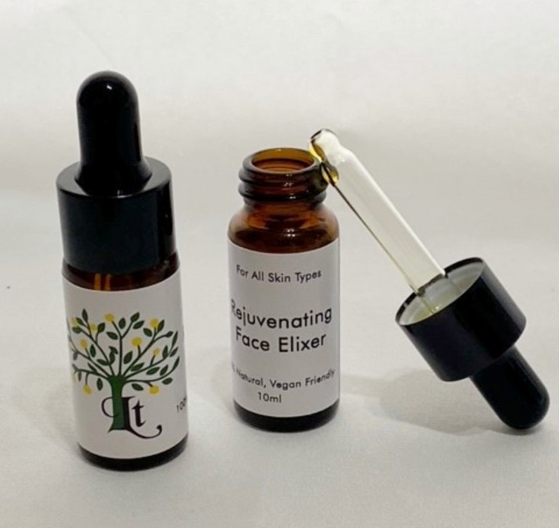 May include: Two amber glass bottles with black dropper tops. The bottle on the right has a clear dropper and is labelled "Rejuvenating Face Elixir" with the text "For All Skin Types", "Natural, Vegan Friendly", and "10ml".