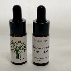 May include: Two small brown glass bottles with black dropper tops and white labels. The label on the right bottle reads "For All Skin Types Rejuvenating Face Elixir 100% Natural, Vegan Friendly 10ml".