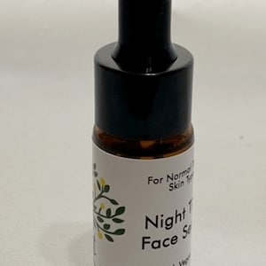 May include: A small amber glass bottle with a black dropper top. The bottle has a white label with the text "For Normal Skin Types", "Night Time Face Serum", "100% Natural, Vegan", and "10 ml".
