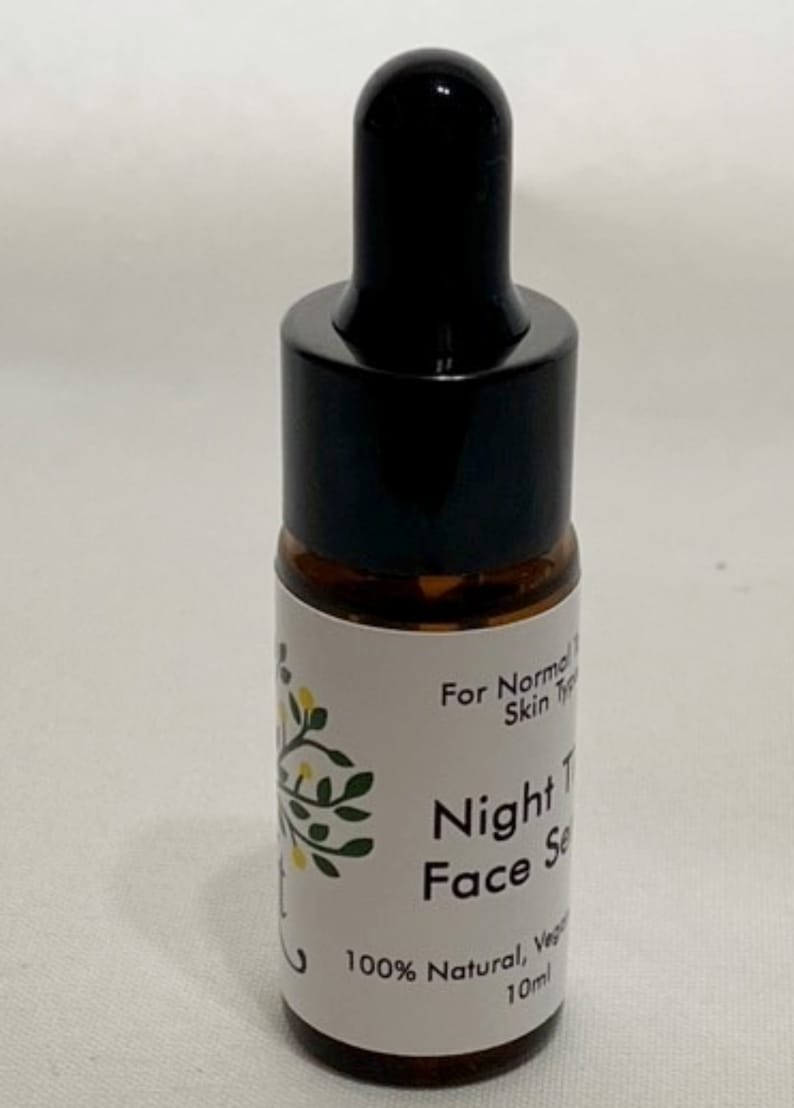 May include: A small amber glass bottle with a black dropper top. The bottle has a white label with the text "For Normal Skin Types", "Night Time Face Serum", "100% Natural, Vegan", and "10 ml".