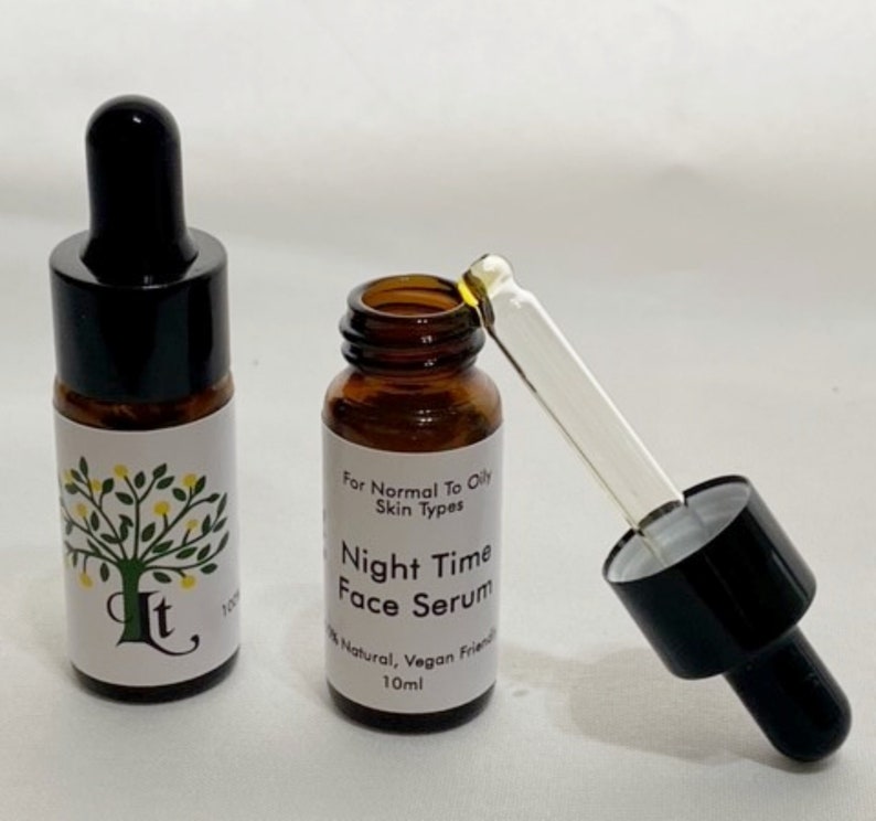 May include: Two amber glass bottles with black dropper tops. The bottle on the right has a dropper attached. Both bottles have white labels with a green tree and the text "It" and "Night Time Face Serum". The label on the right bottle also includes the text "For Normal To Oily Skin Types", "100% Natural, Vegan Friendly", and "10ml".