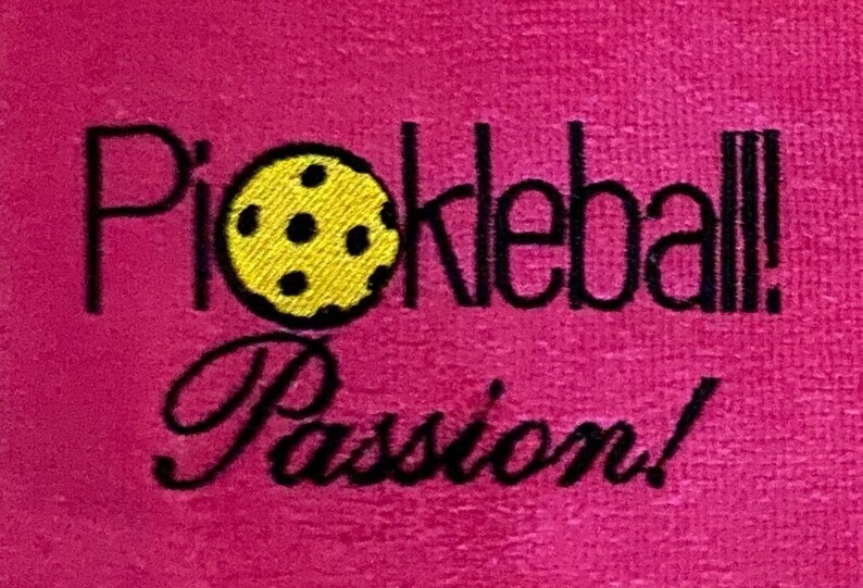 May include: Pink towel with black embroidery that reads "Pickleball! Passion!" with a yellow pickleball in the center.