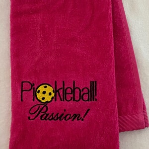 May include: A pink towel with the text "Pickleball Passion!" embroidered in black with a yellow pickleball graphic.