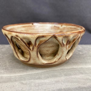 May include: A small, brown and white ceramic bowl with a unique, openwork design. The bowl has a rounded shape and a slightly flared rim.