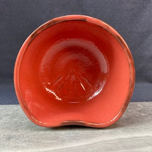 May include: A red ceramic bowl with a slightly wavy rim. The bowl has a smooth, glossy finish and a subtle indentation in the center.