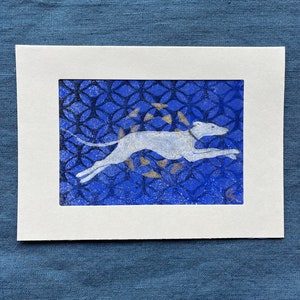 Könnte beinhalten: Ein weißer Hund, der auf einem blauen Hintergrund mit einem gold-blauen Muster läuft. Der Hund ist in der Luft und seine Beine sind ausgestreckt. Der Hintergrund ist ein sich wiederholendes Muster aus Kreisen und Ovalen.