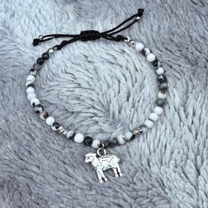 Puede incluir: Pulsera de cuentas moteadas blancas, grises y negras. Cuenta con un dije de oveja plateado. El cordón negro ajustable permite un ajuste cómodo. Un accesorio único.