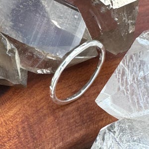 May include: A silver ring with a textured band, resting among clear quartz crystals. The ring's surface reflects light, highlighting its delicate design. The ring is a piece of jewelry.