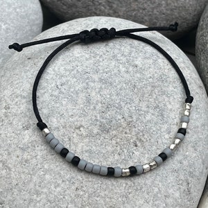 Puede incluir: Un brazalete de cuerda negra con cuentas grises y plateadas.