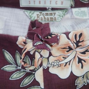 May include: A maroon and white patterned fabric with a floral design. The fabric has a brown drawstring with a bow. The fabric has a label that says "Tommy Bahama" and "Stretch".