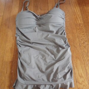 May include: A grey swimsuit with a ruched bodice and a ruffled hem.