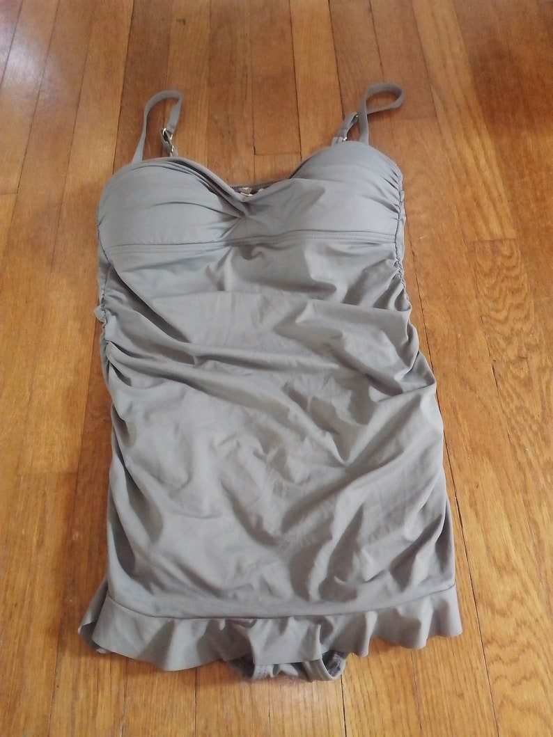 May include: A grey swimsuit with a ruched bodice and a ruffled hem.