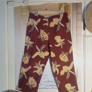 May include: A pair of maroon cropped pants with a tropical print featuring yellow and green leaves and flowers.
