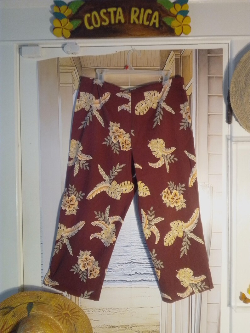 May include: A pair of maroon cropped pants with a tropical print featuring yellow and green leaves and flowers.