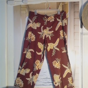 May include: A pair of maroon pants with a tropical print featuring yellow and green leaves and flowers.