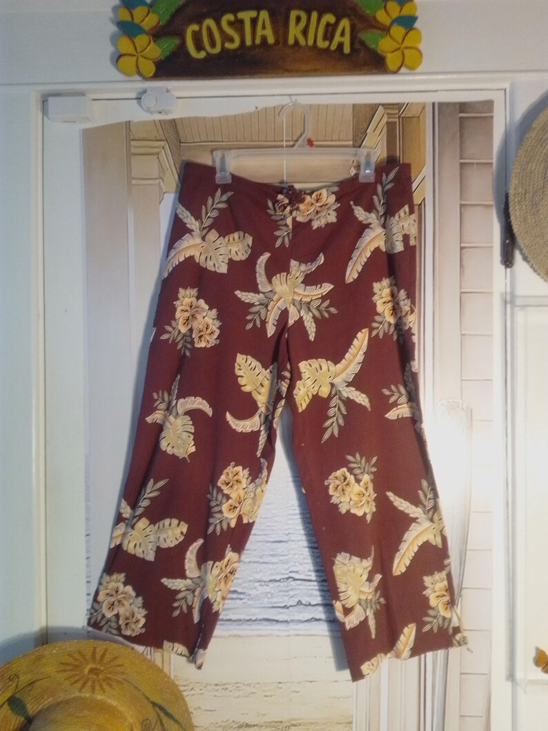 May include: A pair of maroon pants with a tropical print featuring yellow and green leaves and flowers.