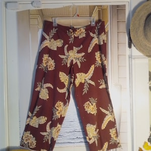 May include: A pair of maroon pants with a tropical print featuring yellow flowers and green leaves.