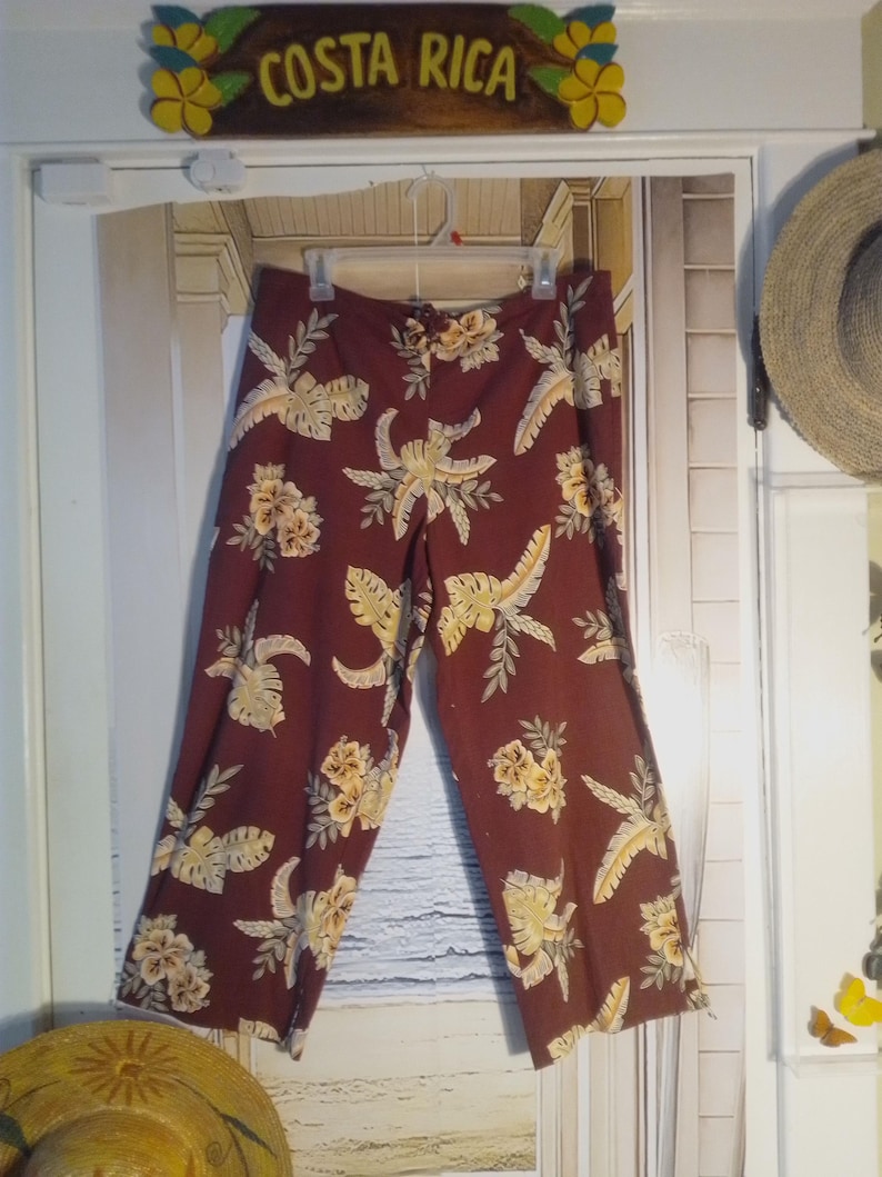 May include: A pair of maroon pants with a tropical print featuring yellow flowers and green leaves.