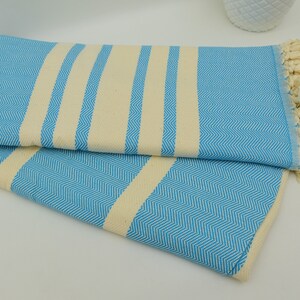 May include: A blue and white striped Turkish towel with fringe. The towel is folded in half and has a herringbone pattern.