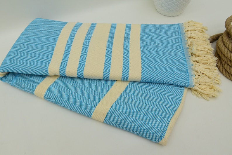May include: A blue and white striped Turkish towel with fringe. The towel is folded in half and has a herringbone pattern.
