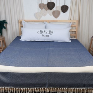 May include: A blue and white throw blanket with fringe on the bottom edge. The blanket is on a bed with white pillows and a pillow with the text "Mr. & Mrs. Est. 2015".