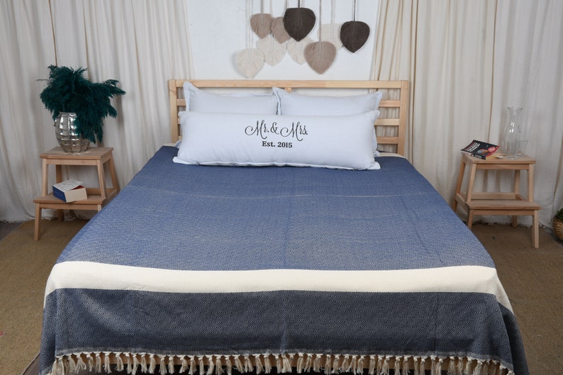 May include: A blue and white throw blanket with fringe on the bottom edge. The blanket is on a bed with white pillows and a pillow with the text "Mr. & Mrs. Est. 2015".