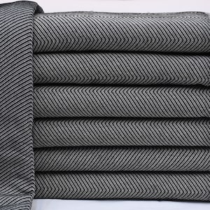 May include: A stack of six folded blankets with a black and white chevron pattern. The blankets have a fringe on the edge. The blankets are made of a soft material and are neatly stacked on top of each other.