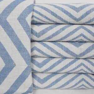 May include: A stack of folded blue and white chevron patterned towels. The towels have a light blue and white zigzag design. The edges of the towels have a fringe detail. The towels are made of a soft, woven material.