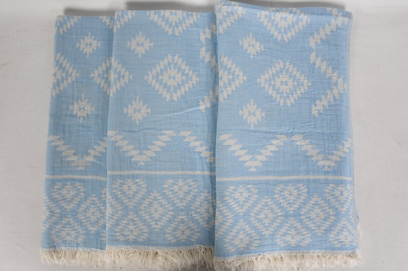 Pu&ograve; includere: Quattro asciugamani di colore azzurro chiaro con un motivo geometrico bianco. Gli asciugamani hanno un bordo a frangia.