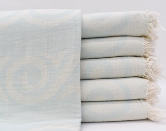 May include: A stack of light blue Turkish towels with white fringe. The towels are folded and stacked on a white surface.