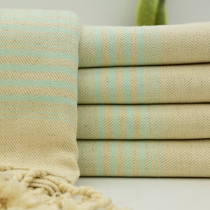 May include: A stack of light beige towels with thin, light blue stripes. The towels have fringe on the ends.