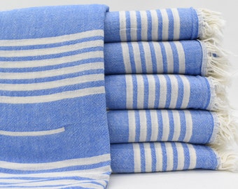 May include: A stack of six blue and white striped towels with white fringe. The towels are folded and stacked on a white surface.