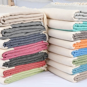 May include: A stack of Turkish towels in various colors, including beige, dark gray, navy blue, fuchsia, black, red, pistachio green, light gray, seafoam green, brown, orange, turquoise, dark green, dark turquoise, and light brown.
