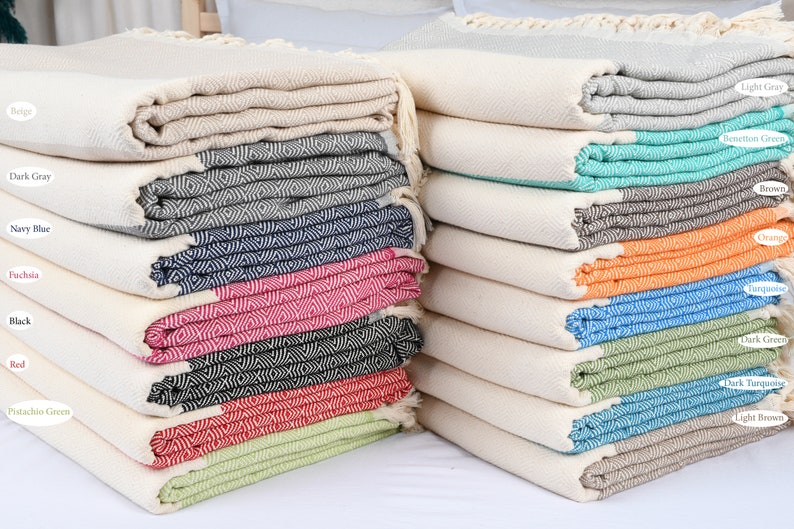 May include: A stack of Turkish towels in various colors, including beige, dark gray, navy blue, fuchsia, black, red, pistachio green, light gray, seafoam green, brown, orange, turquoise, dark green, dark turquoise, and light brown.