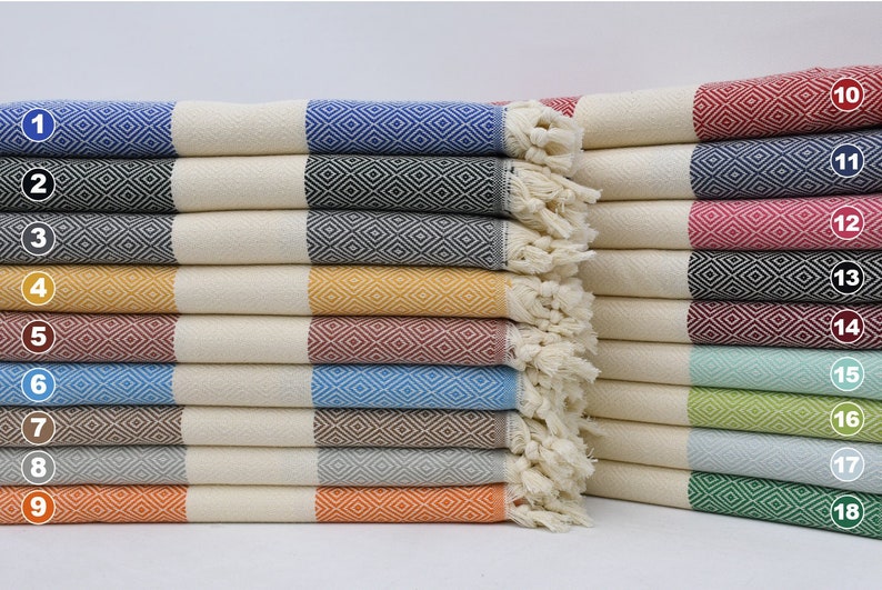 May include: A stack of 18 Turkish towels, each with a different colour and pattern. The towels are folded and stacked in a row, with the numbers 1 through 18 visible on the side.
