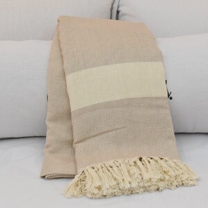 May include: A beige throw blanket with a diamond pattern and a white stripe. The blanket has a fringe border.