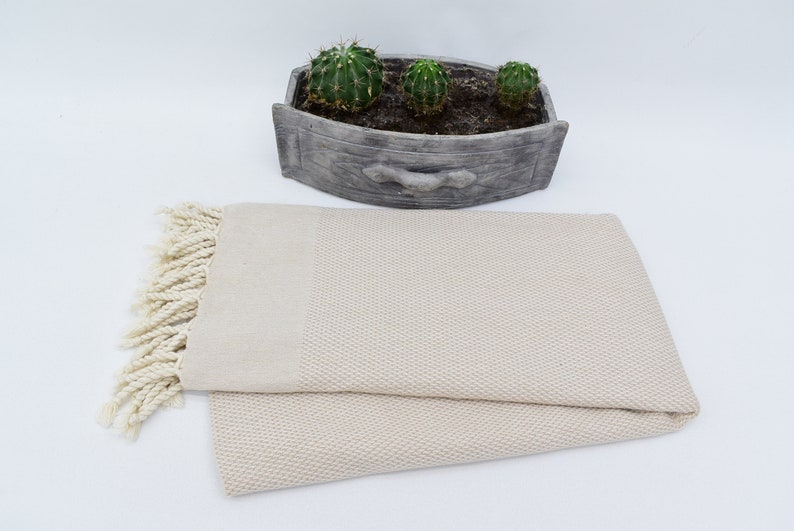 May include: A cream-coloured Turkish towel with fringe on the ends. The towel is folded in half and has a waffle-like texture.